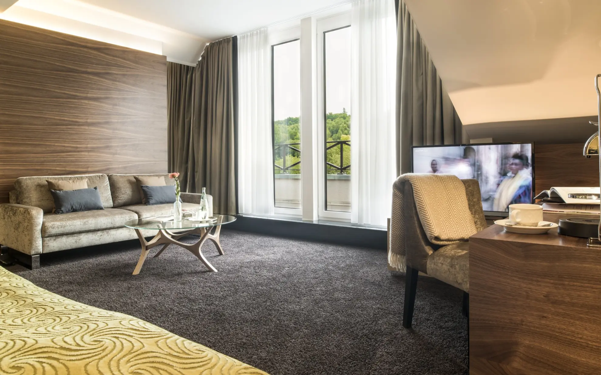 Juniorsuite mit Dachschraege Couch Schreibtisch Doppelbett und gruener Tagesdecke