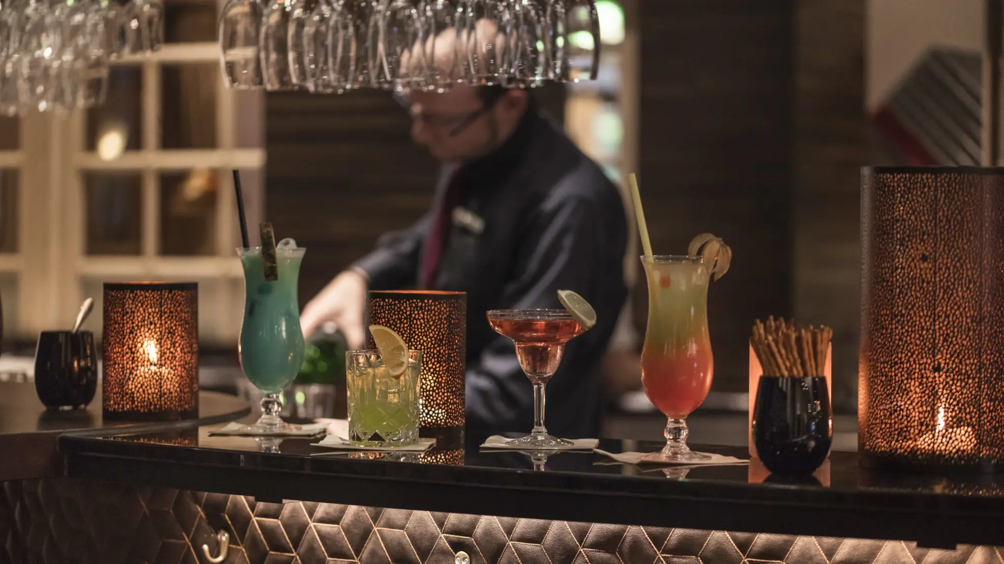 Hotelbar Birdie in Abendstimmung beleuchtet Barkeeper bereitet Getraenke vor bunte Cocktails im Vordergrund