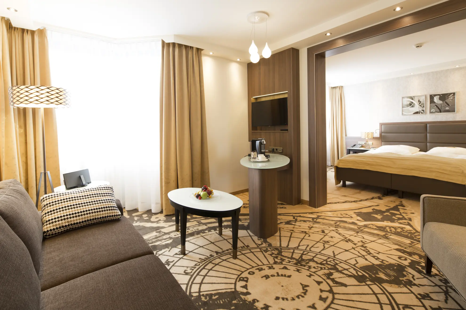 Juniorsuite in Beigetoenen mit Couch Tischen Stehlampe TV Doppelbett und Teppich mit Globus Motiv 2