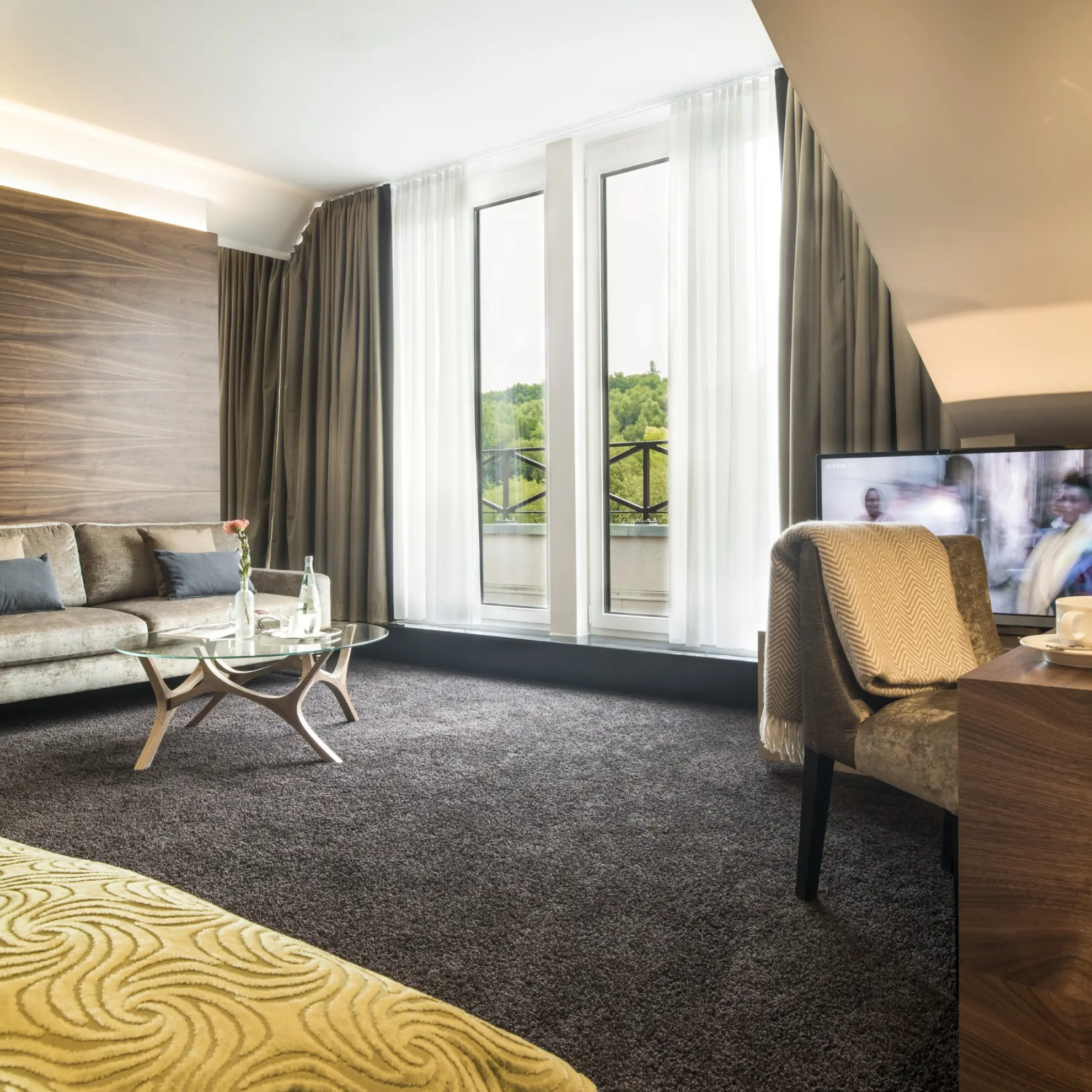 Juniorsuite mit Dachschraege Couch Schreibtisch Doppelbett und gruener Tagesdecke