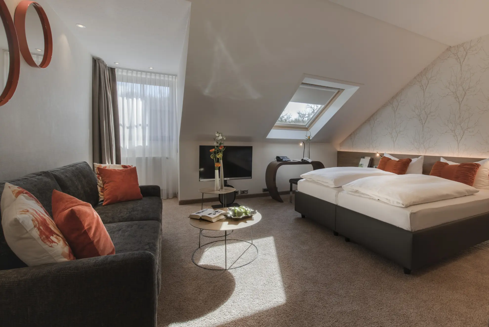 Komfort Plus Doppelzimmer mit Dachschraege Doppelbett Tisch Couch TV und helle Tapete mit Zweigen